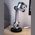 Metallic piston desk lamp on a wooden surface with a computer monitor in the background