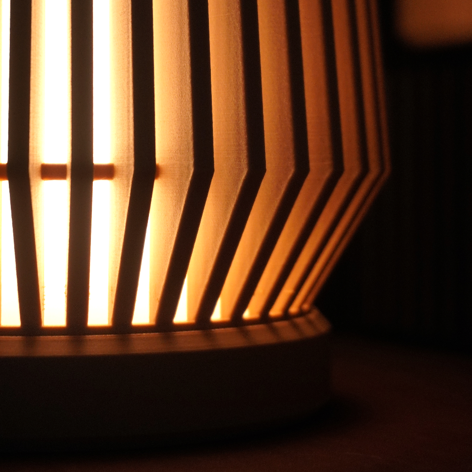 Close-up of a modern vertical slat lamp glowing with warm orange light, showing the illuminated gaps between dark wooden or metal bars.