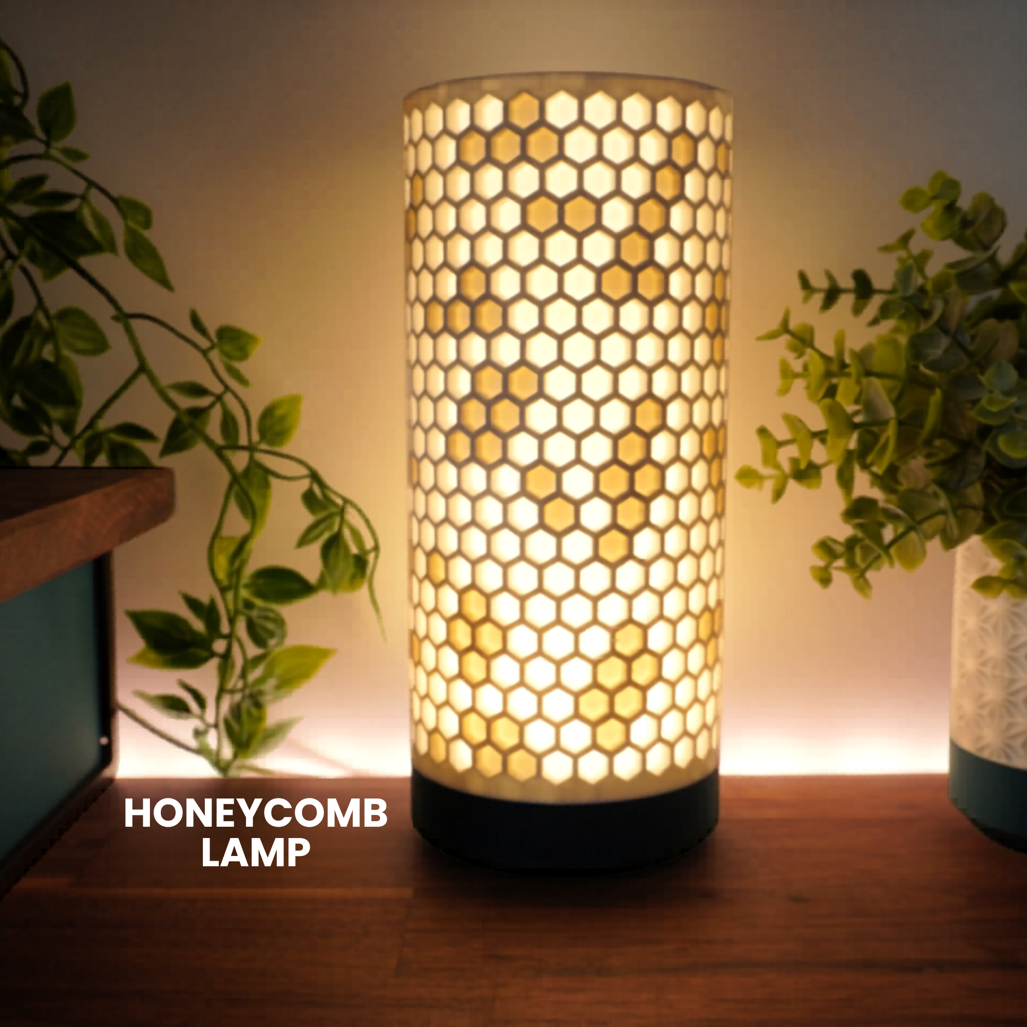A cylindrical table lamp with a glowing honeycomb pattern on a warm white shade, set on a wooden surface with houseplants in the background. Text overlay reads 'HONEYCOMB LAMP'.