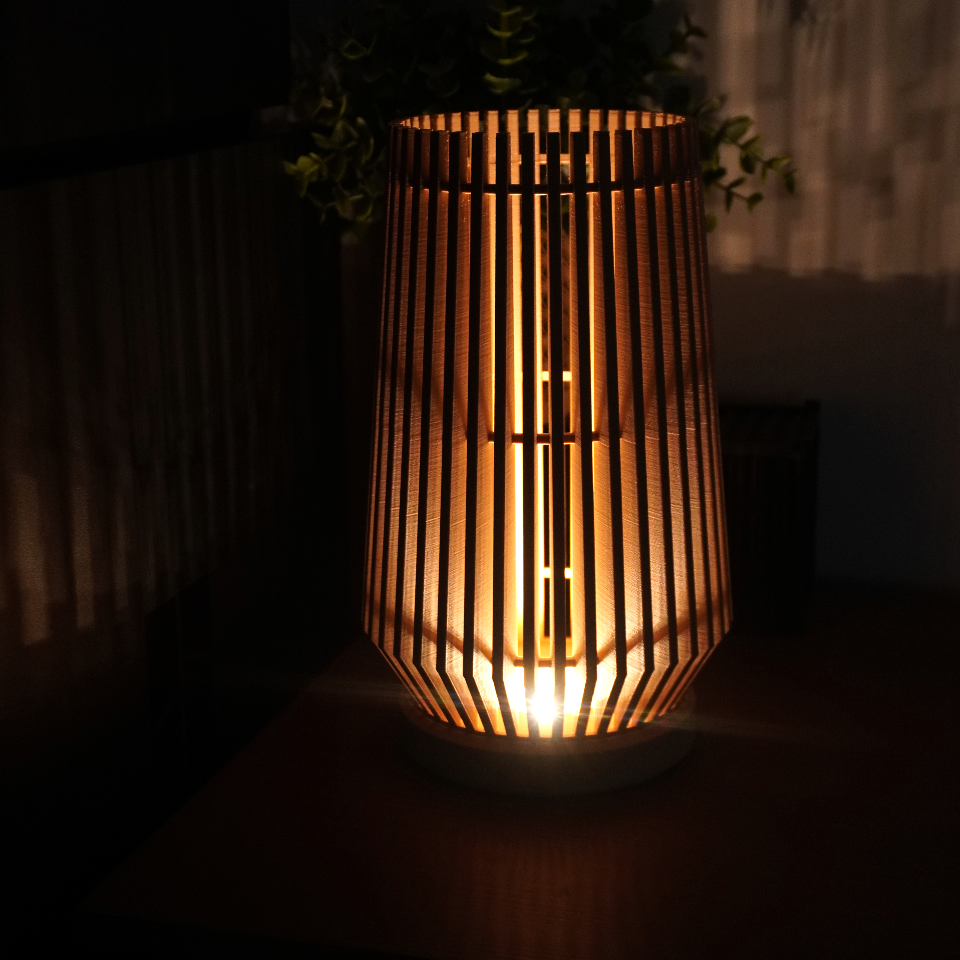 A modern bamboo slat table lamp glowing with warm light, set against a dark background with soft shadows.