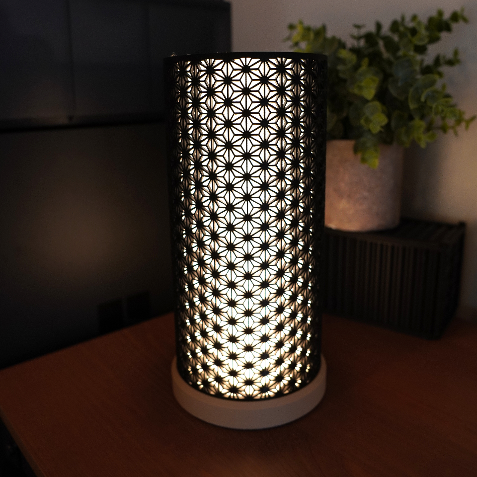 Decorative lamp with intricate pattern on a wooden surface in a dimly lit room.