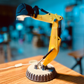 Yellow robot arm model on a wooden surface with a blurred indoor background