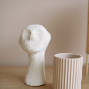 A simple composition of a ceramic figurine and a textured vase on a wooden surface.